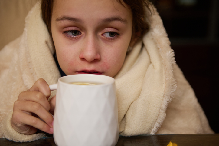 Young child bundled in blanket holding a warm drink during winter cold